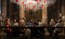 The cast of "Glass Onion" sits around a long dining room table. 