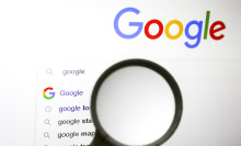 A magnifying glass is held up to a screen showing the Google homepage.