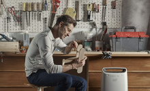 Man in a workshop crafting a toy, next to a dehumidifier