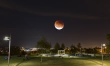 A dim, reddish moon seen over a park at night