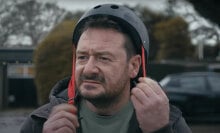 A middle-aged man puts on a skateboard helmet.