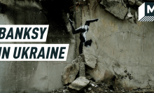 A mural painting depicts a female gymnast balancing a headstand on top of buildings ruins. Caption reads: "Banksy in Ukraine"