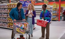 Three people dressed in '80s clothes stand in a bright, clean supermarket.