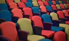 Several rows of seats in a theatre. The seats have armrests either side and are tightly packed together. 