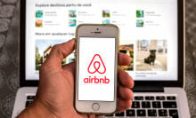 The Airbnb app seen displayed on a smartphone screen with the Airbnb website displayed on a laptop in the background.