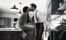 A couple kiss in their kitchen.
