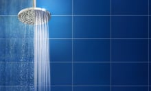 Water streaming from shower head against backdrop of teal blue tiles.