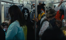 A person wearing a creepy ghost mask stands in a crowded subway. 
