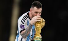 A footballer wearing an Argentina uniform kisses the World Cup trophy.