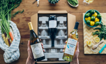 hands holding two bottles of wine with box from firstleaf and food on counter