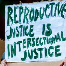 Protest sign that says "Reproductive Justice is Intersectional Justice" in green lettering. 