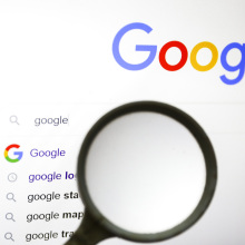 A magnifying glass is held up to a screen showing the Google homepage.
