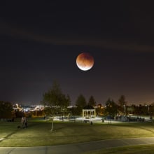 A dim, reddish moon seen over a park at night