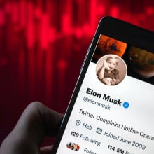 Elon Musk's Twitter handle on a smartphone against a red line declining steeply. 