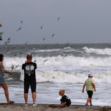 a family seen from behind as they stand on a beach watching rough seas.