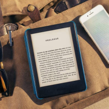 An e-reader called the Amazon Kindle is placed on a surface with some text on its display
