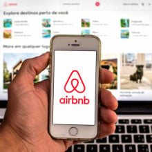 The Airbnb app seen displayed on a smartphone screen with the Airbnb website displayed on a laptop in the background.