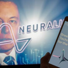 The Neuralink website displayed on mobile phone with founder Elon Musk seen on screen in the background.