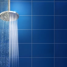 Water streaming from shower head against backdrop of teal blue tiles.