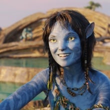 A blue Na'vi alien girl sits by the ocean.