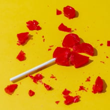Front view of broken heart-shaped lollipop on a yellow colored background
