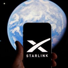 The Starlink logo on a smartphone, in front of an image of the Earth from space.