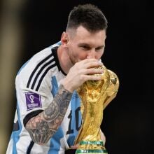 A footballer wearing an Argentina uniform kisses the World Cup trophy.
