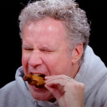 A man eats a chicken wing while closing his eyes in apparent discomfort.