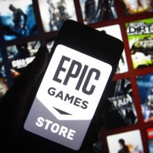 Epic Games Store logo on a phone with a background collage of blurry game cover art