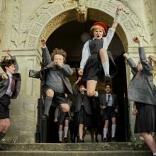 Kids in school uniform jump out of a school.