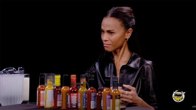 A woman sits at a table with a row of hot sauces in front of her.