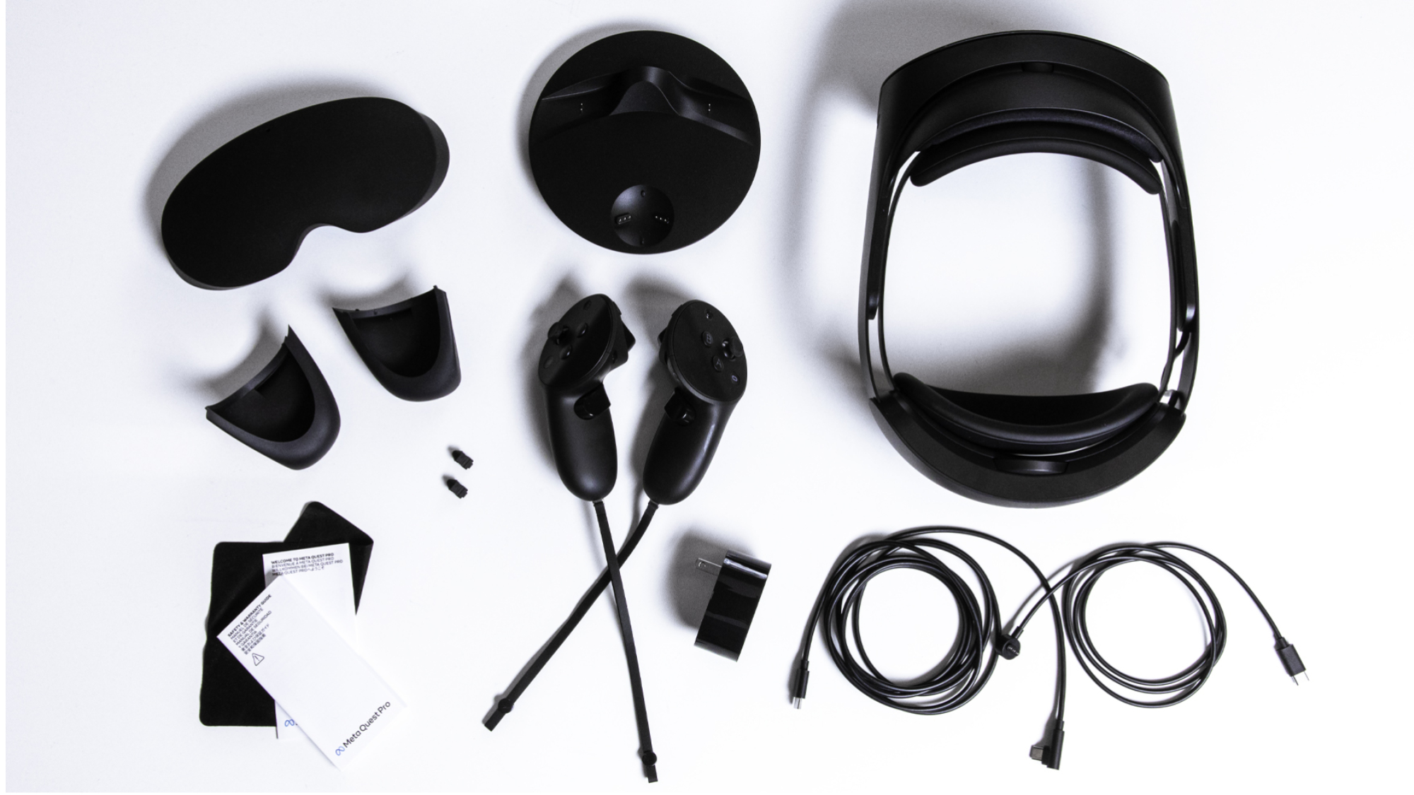 A flat lay of the Quest Pro's accessories: a protective rubber cover for the headset's glass panel, a charging doc, cords, and wall charger, two controllers, magnetic gaskets, two stylus tips, a glass cleaning cloth, and a small manual.
