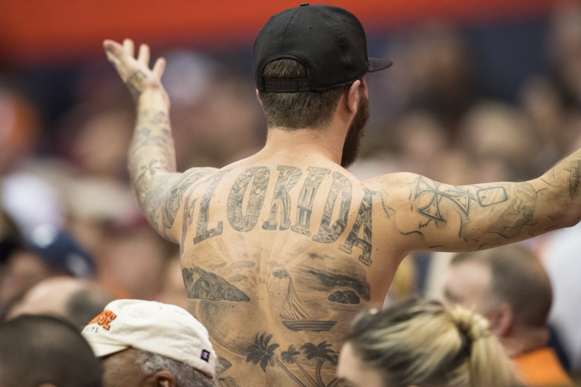The bare back of a white man who is being held up above a crowd. The word "Florida" has been tattooed in large capital letters across his shoulder blades.