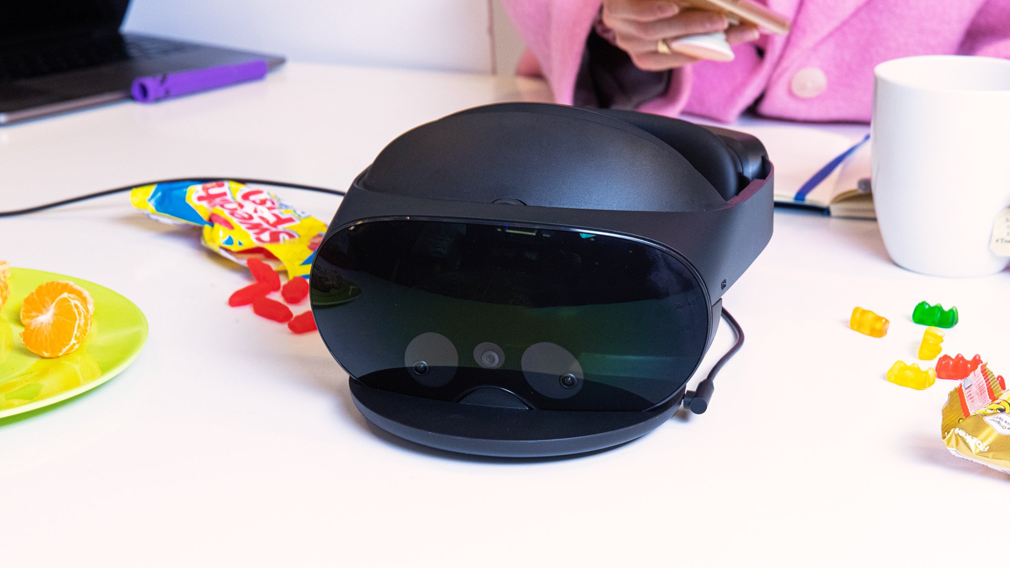 The Quest Pro from the front, charging in its dock. It is surrounded by opened Swedish Fish and Haribo packets.