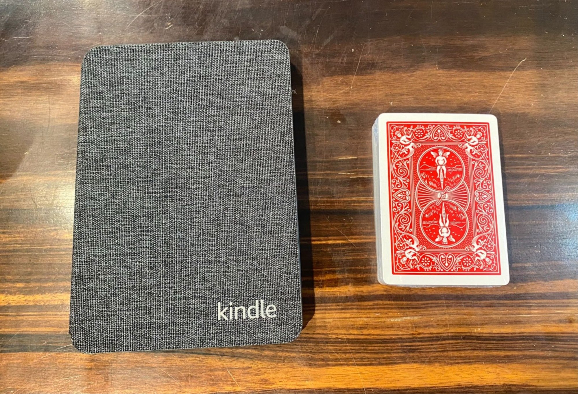 kindle next to a deck of playing cards to show how compact the kindle is