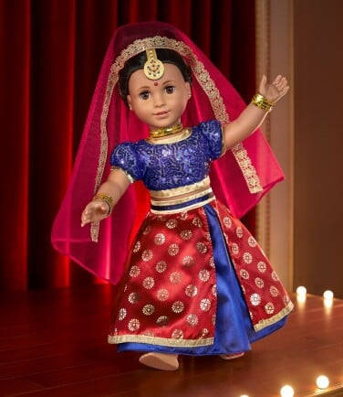 The Kavi doll is dressed in brightly-colored traditional Indian dress and performing a dance on a lit-up stage. 
