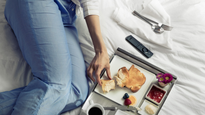 Body of person lying down reaching for food from tray on bed