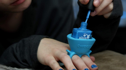 Person painting nails blue with polish in ring holder on hand