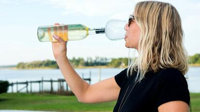 person drinking from sleeve attached to wine bottle