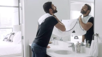 a man shaving in front of a bathroom mirror using a beard bib