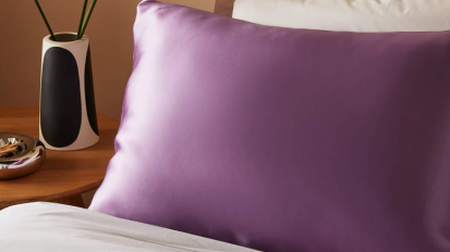 a purple mulberry silk pillowcase on a bed next to a vase filled with leafy branches
