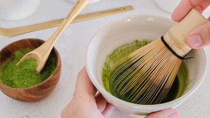 a close-up of a person whisking matcha tea