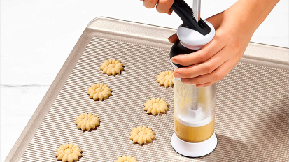 a close-up of a person making christmas cookies using an oxo cookie press 