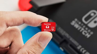 a close-up of a person holding a microsd card in front of a nintendo switch