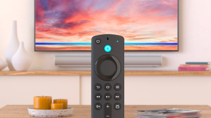 a close-up of an alexa voice remote being held up in front of a tv in a living room